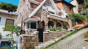 A two-story house with a stone facade, a red-tiled roof, and a staircase leading to the entrance.