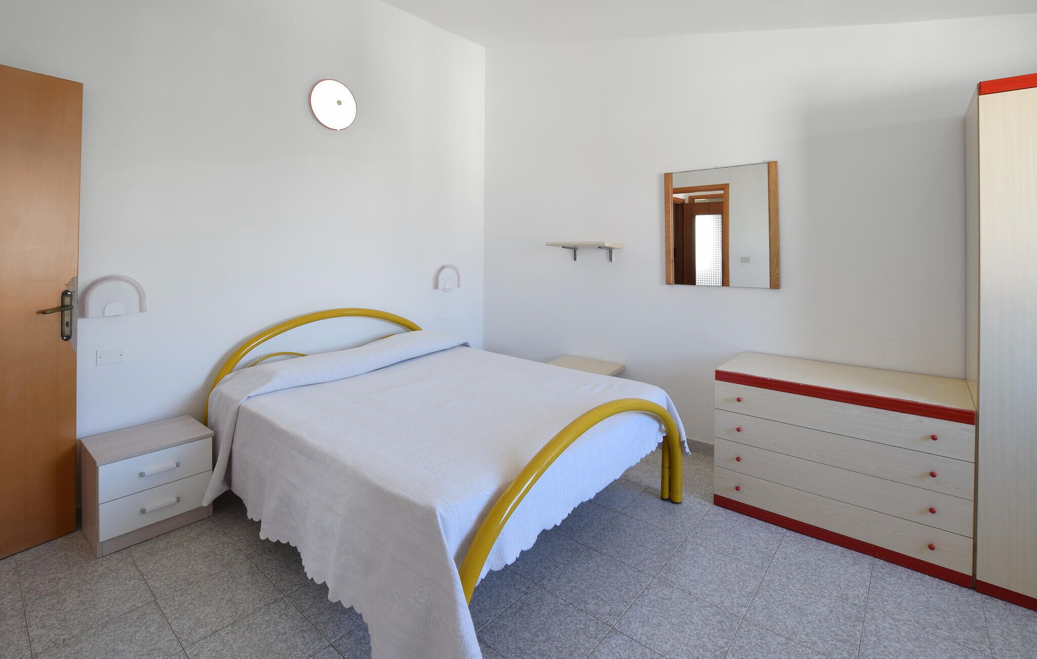 Une chambre à coucher avec un lit, des tables de chevet, une commode, un miroir et une porte.