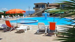 A swimming pool with lounge chairs and umbrellas, a fountain, and a building with a staircase. - 1 bedroom gorgeous apartment in Briatico (Briatico)