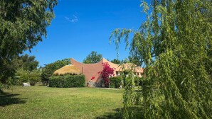 Een huis met rieten dak, omgeven door een verzorgd gazon en diverse bomen.