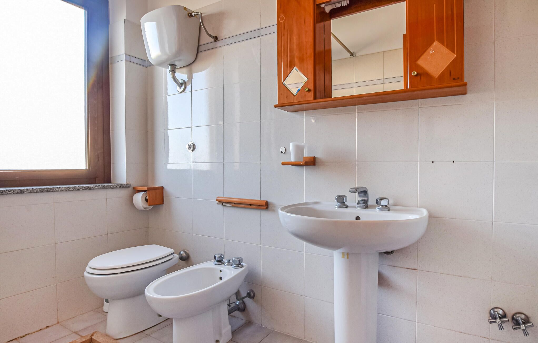 Une salle de bain comprenant des toilettes, un bidet, un lavabo et un meuble avec miroir.