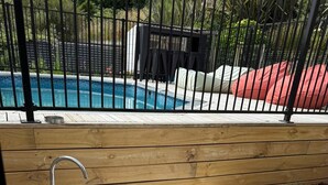 Eine Holzterrasse mit einer eingebauten Badewanne, einem Metall-Wasserhahn und einem Pool im Hintergrund.