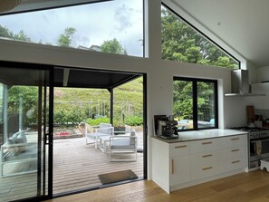 A modern kitchen with a large window, a dining area with white furniture, and a view of the garden.