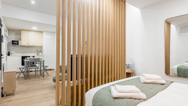 A modern hotel room with a wooden partition, a bed with a green blanket, a bedside table, and a view into the kitchen area. - Chueca Center II - Studio for 4 in downtown Madrid (Madrid)