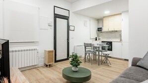 A modern living room with a grey sofa, a round green coffee table with a plant, and a dining area with a white table and chairs. - Chueca Center II - Studio for 4 in downtown Madrid (Madrid)