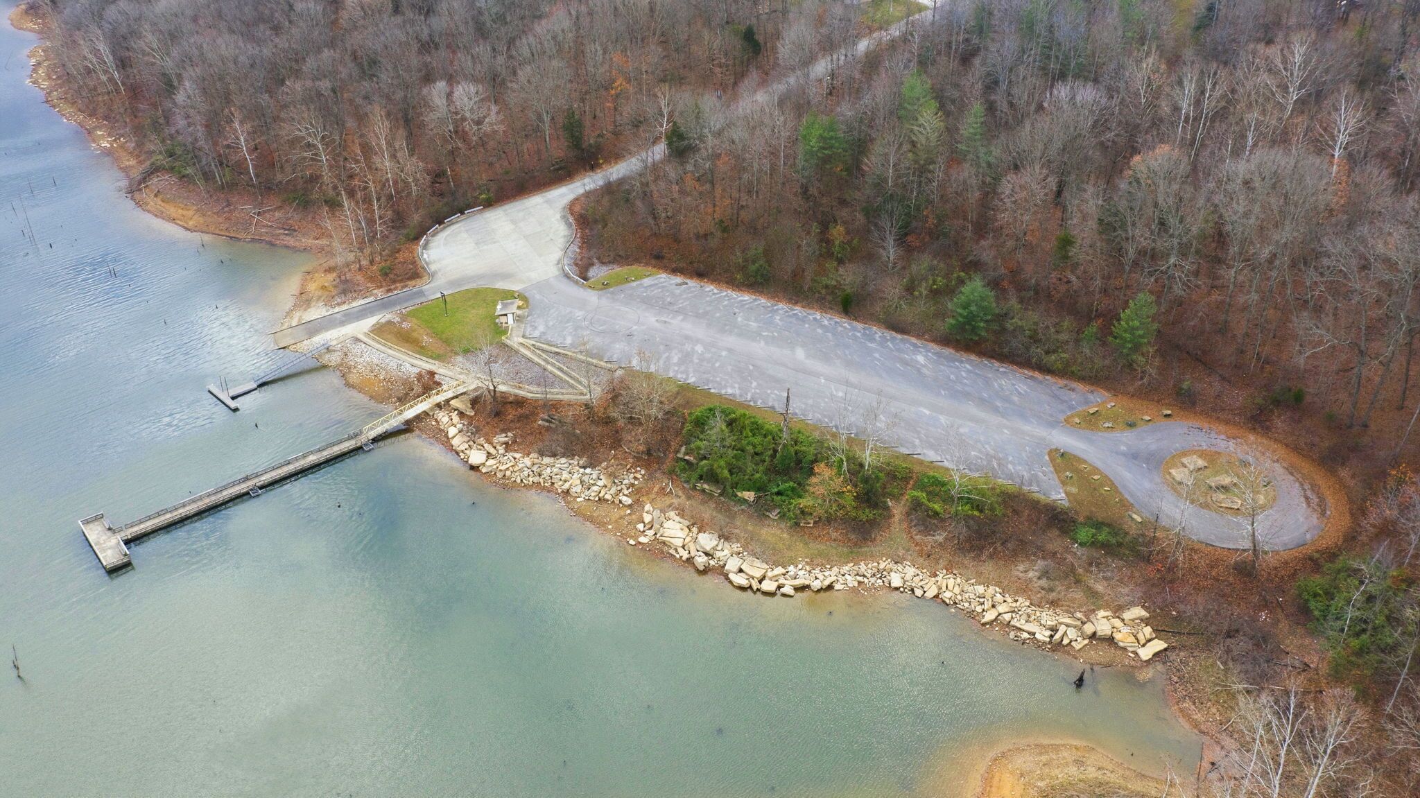 Vue aérienne d’une zone au bord d’un lac, avec une route asphaltée, un quai et un petit bâtiment.