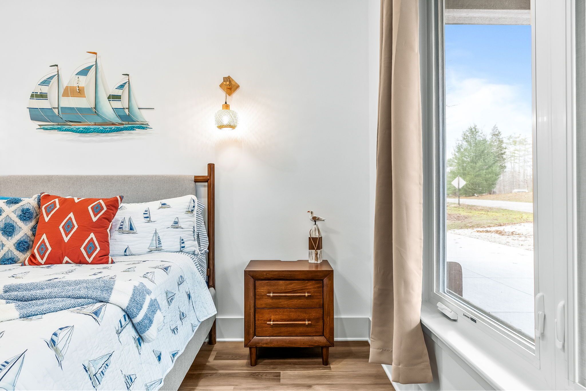 Une chambre à coucher comprenant un lit, une table de chevet, une lampe fixée au mur et une fenêtre avec des rideaux.