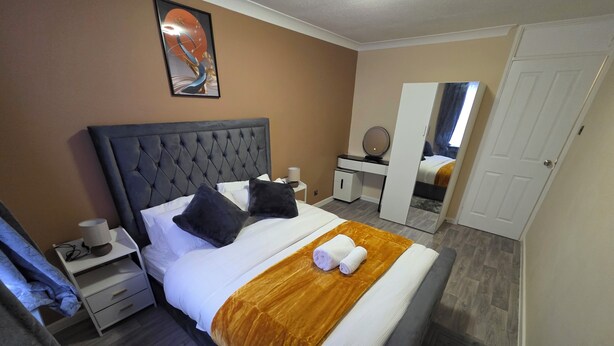 Una habitación de hotel ordenada con una cama grande, una mesita de noche, un espejo y un armario.