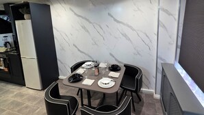 Un área de comedor moderna con una pared de mármol, una mesa vestida en blanco y negro, y una cocina al fondo.