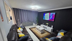 Una sala de estar moderna con dos sofás de cuero negro, una mesa de centro blanca y un televisor de pantalla plana montado en la pared.