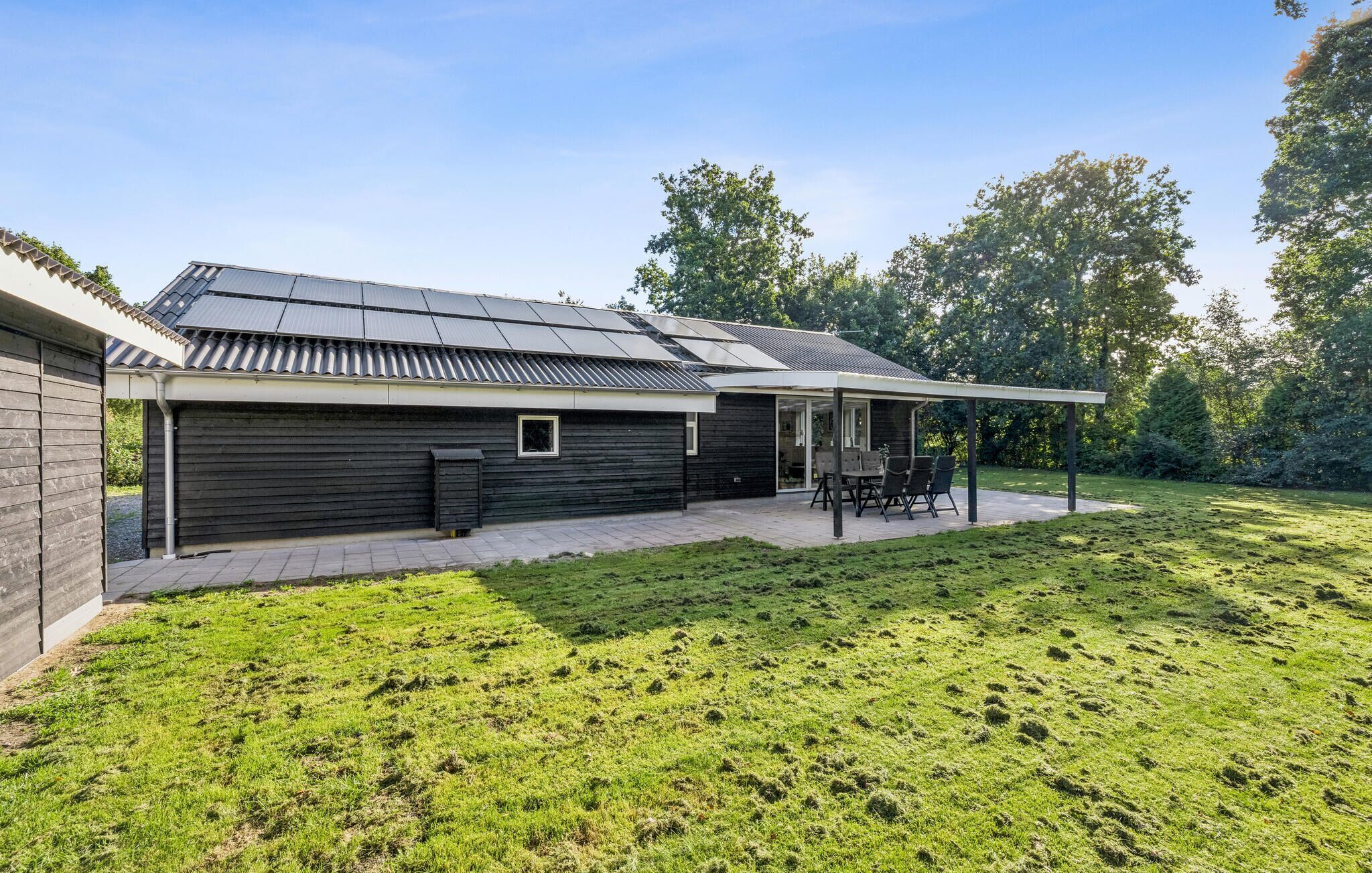 Ein modernes Haus mit überdachter Terrasse, Solaranlage und Rasengarten.