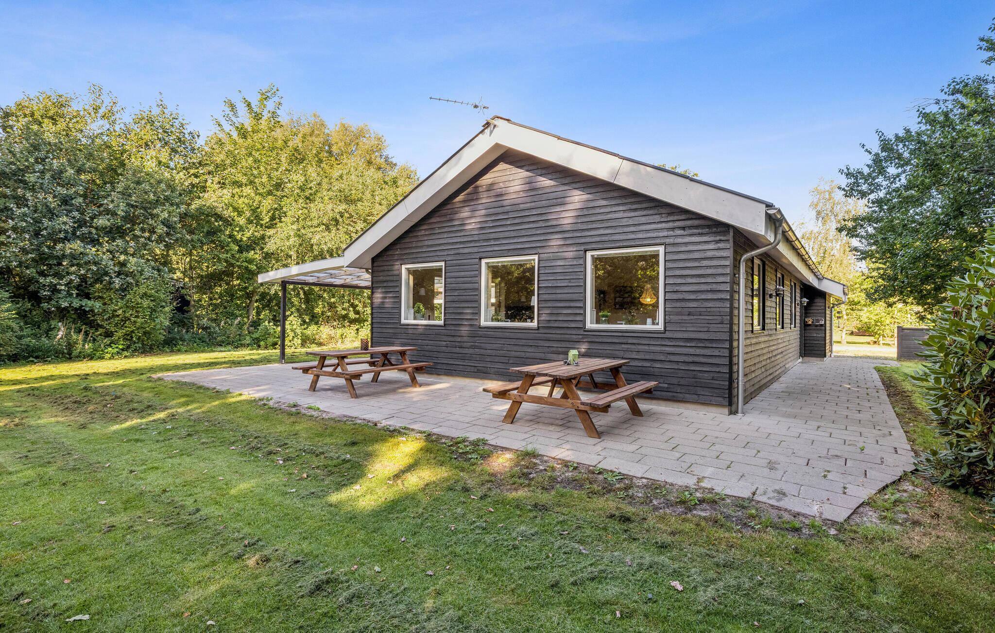 A modern wooden cabin with a patio area, picnic tables, and a covered seating area.