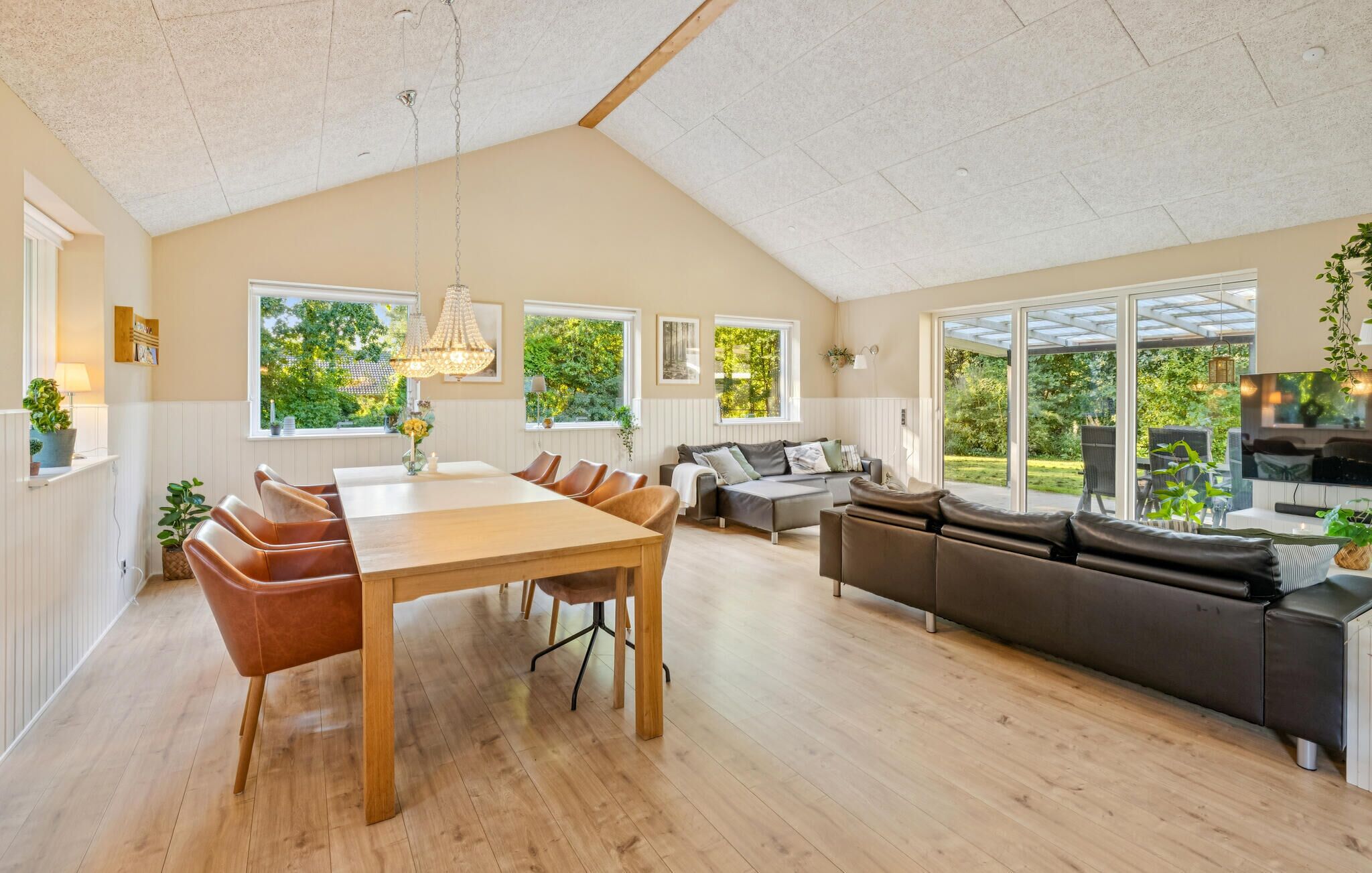A spacious living area with a dining table, sofas, and large windows offering a view of greenery.