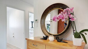 A wooden vanity with a round mirror, a vase with pink orchids, and a potted plant. - Seaside Premium Home with Spa Pool near Beach (Auckland East)