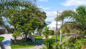 A residential area with a large tree, a white house, and a clear view of the ocean. - Seaside Premium Home with Spa Pool near Beach (Auckland East)