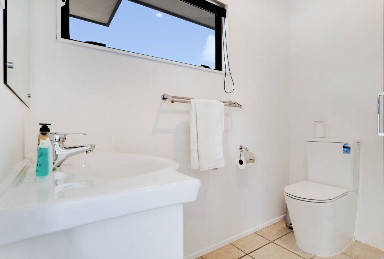 A bathroom with a white sink, a toilet, and a window above the sink.