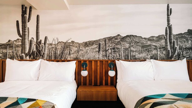 Une chambre d’hôtel avec deux lits, une tête de lit en bois et une fresque murale sur le thème du désert.