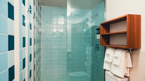 Une salle de bain avec une douche à parois de verre, des toilettes et une étagère en bois où sont rangés les articles de toilette.