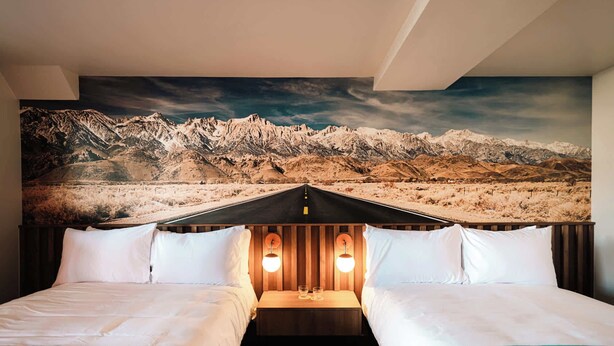 A hotel room with two beds, a mountain view mural, and a wooden headboard with lights. - Desert Mirage Room | La Vista Motel | 104 (Denver)