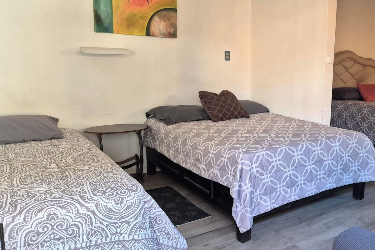 A hotel room with two beds, each with patterned bedding and a headboard. There is a small bedside table and a chair in front of one bed.