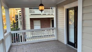 A covered porch with a patterned floor, a white railing, and a hanging light fixture.