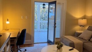 A living room with a sofa, a round coffee table, a desk with a chair, and a door leading to a balcony.