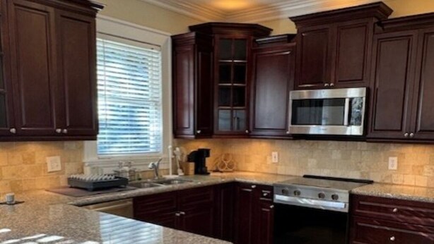 A kitchen with dark wood cabinets, a granite countertop, stainless steel appliances, and a window with blinds.
