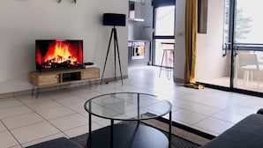 Uma sala de estar moderna com televisão exibindo uma lareira, uma mesa de centro de vidro e um sofá.