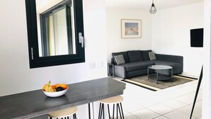 Uma cozinha moderna com bancada preta, dois bancos e uma tigela de frutas.