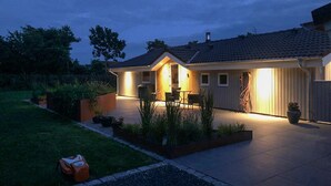 Une maison moderne dotée d’un patio couvert, d’un espace salon extérieur et d’un jardin bien entretenu.