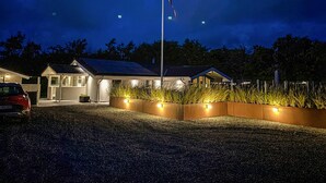Une maison d’habitation au crépuscule, avec une allée, un mât pour drapeau et une entrée bien éclairée.