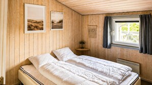 Une pièce comprenant un lit, une petite table, une lampe fixée au mur et une fenêtre avec des rideaux.