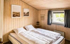Ein Zimmer mit einem Bett, einem kleinen Tisch, einer Wandlampe und einem Fenster mit Vorhängen.