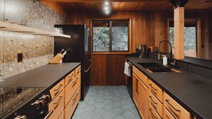 A kitchen with wooden cabinets, a granite countertop, a black refrigerator, and a window with a view of trees. - Huckleberry House At The Yakima River Club! (Easton)