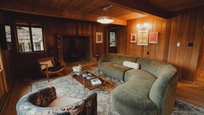A cozy living room with a fireplace, wooden walls, a green sofa, a patterned armchair, and a coffee table. - Huckleberry House At The Yakima River Club! (Easton)