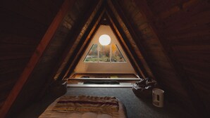 Ein gemütliches Schlafzimmer im Dachgeschoss mit schrägen Wänden, einem Dachfenster, einem Bett und einem Nachttisch.