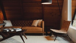 Ein gemütliches Zimmer mit einem braunen Ledersofa, einem gewobenen Sessel und einem Tisch mit Büchern.