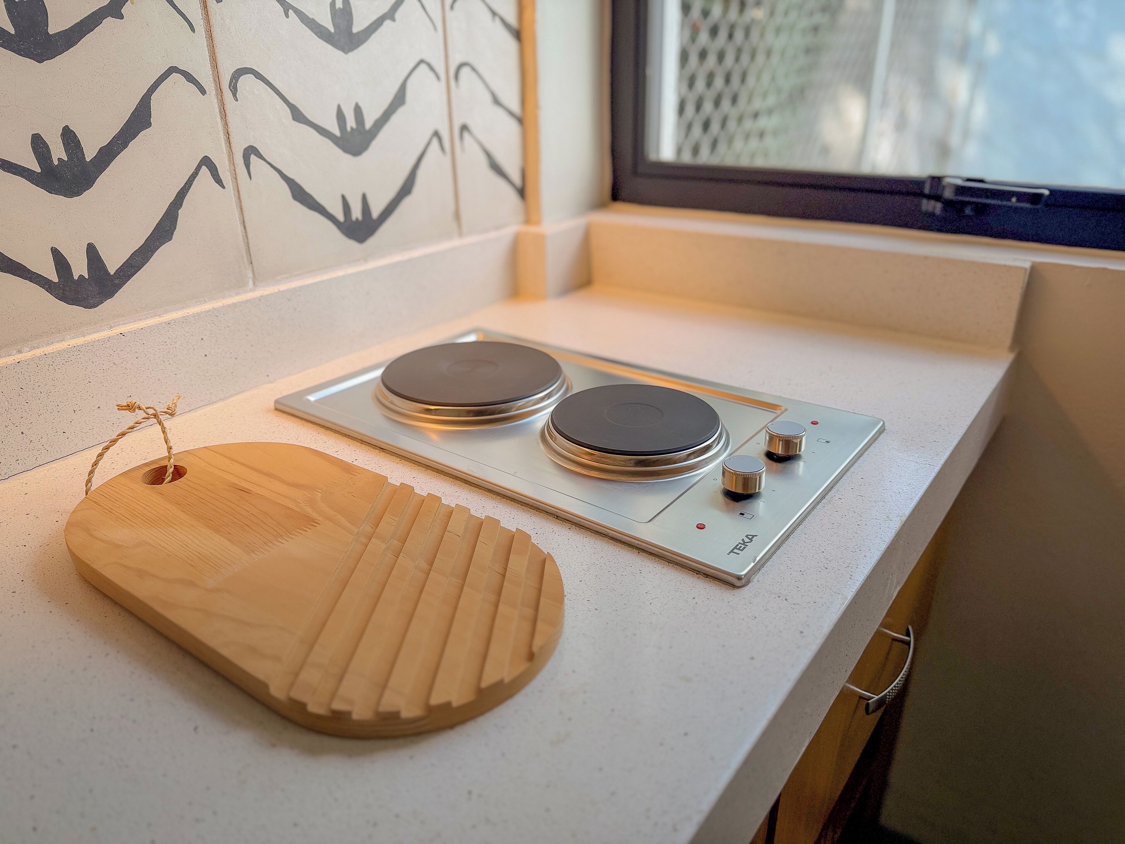 A kitchen with a built-in stove, a wooden cutting board, and a window with a view of the outside.