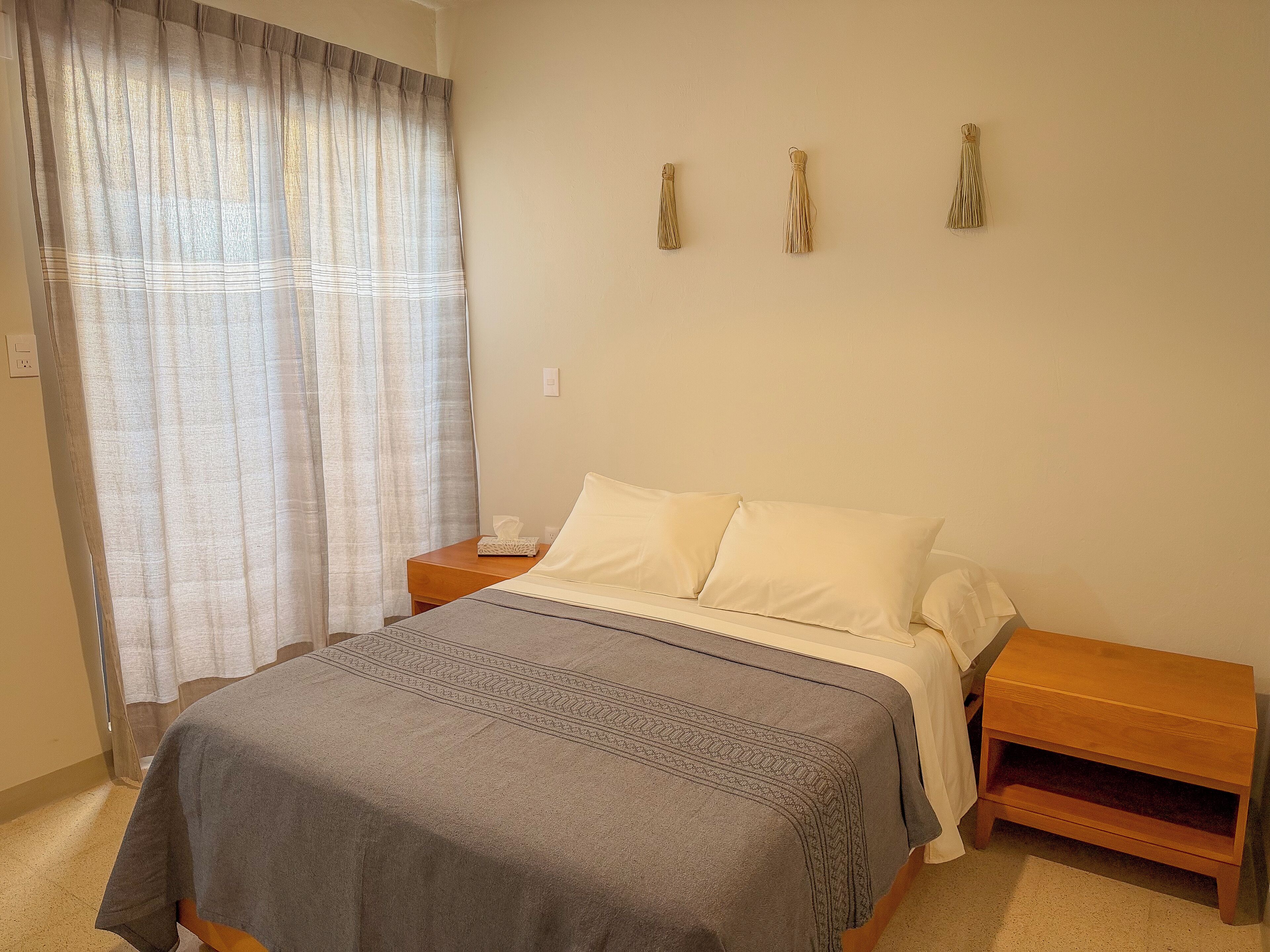 A bedroom with a bed, a nightstand, a wooden bedside table, and a window with curtains.