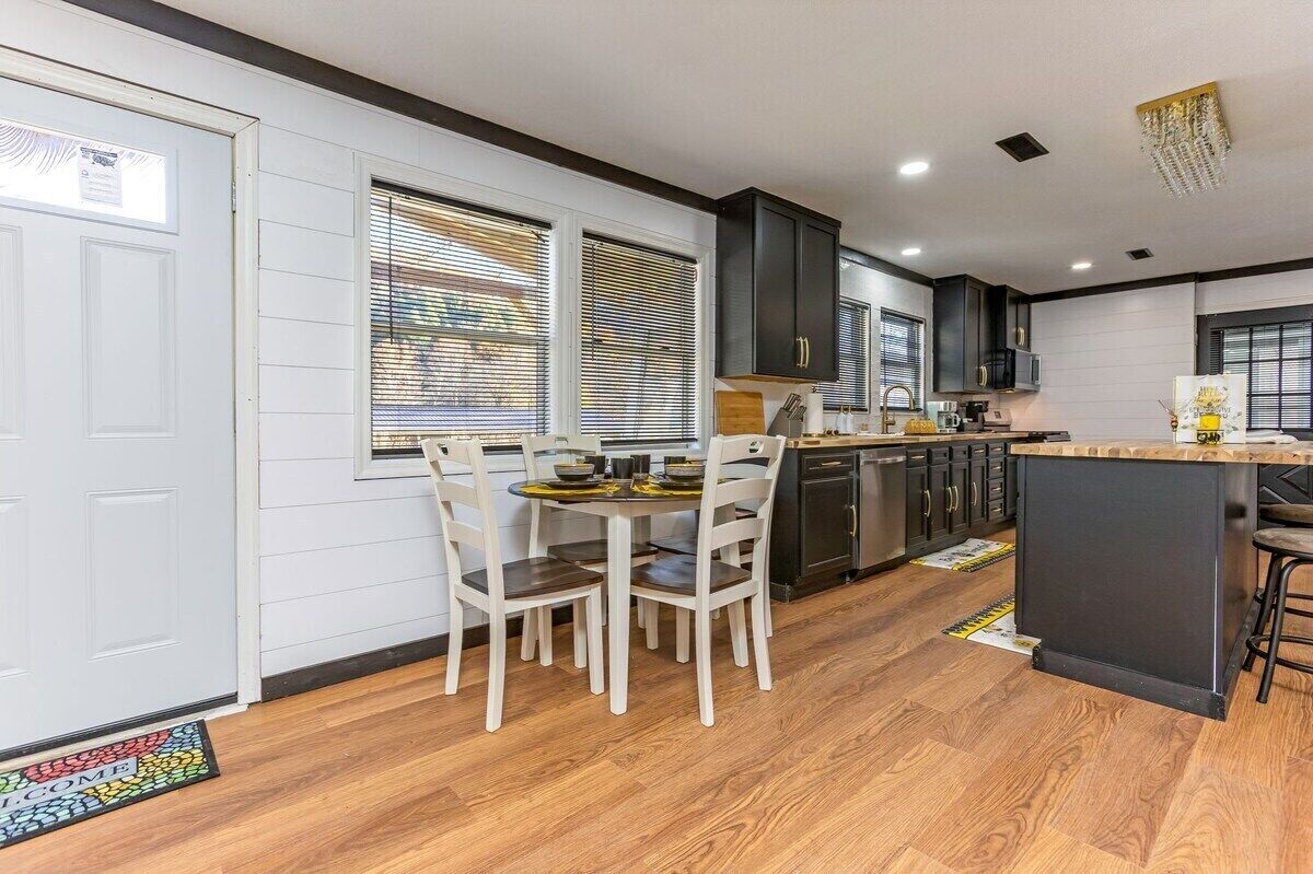 A modern kitchen with dark cabinets, a central island, and a dining area with white chairs.