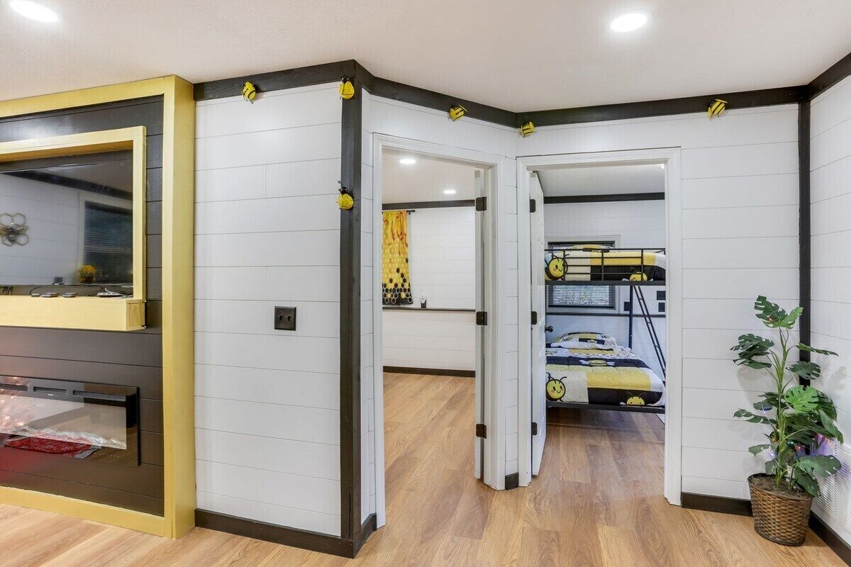 Ein modernes Zimmer mit Küchenzeile, einem Bett mit gelb-schwarzem Überwurf und einem Blumentopf.