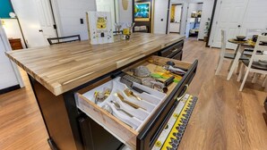 A kitchen with a wooden countertop, a built-in drawer organizer, and a dining area with chairs and a table.