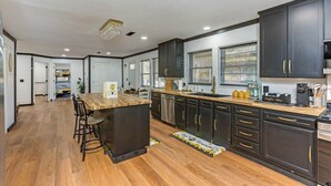 A modern kitchen with dark cabinetry, a wooden island, and a large window.