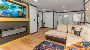 A modern living room with a large flat-screen TV, a beige sofa, and a wooden floor.