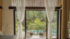 A room with a large glass door leading to an outdoor pool area, a sofa, and a small table. - Ikal Bungalows: HA is a poolside bungalow with AC in a jungle setting of Tulum. (Tulum)