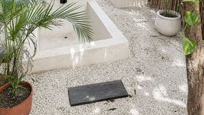A covered outdoor seating area with a cushioned bench, a small planter, and a concrete planter. - Ikal Bungalows: HA is a poolside bungalow with AC in a jungle setting of Tulum. (Tulum)