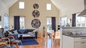 A spacious living area with a sofa, chairs, a coffee table, and a dining table. There are three large circular wall decorations, a window with curtains, and a kitchen area with cabinets and a countertop.