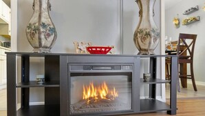 A modern fireplace with a glass front, flanked by two decorative vases, in a room with wooden flooring and a dining area in the background. - Next Stop: Comfort • 3 BR Near Amtrak Station (Richmond)