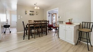 A spacious dining area with a wooden table and chairs, a kitchen island with stools, and a hallway leading to another room. - Next Stop: Comfort • 3 BR Near Amtrak Station (Richmond)