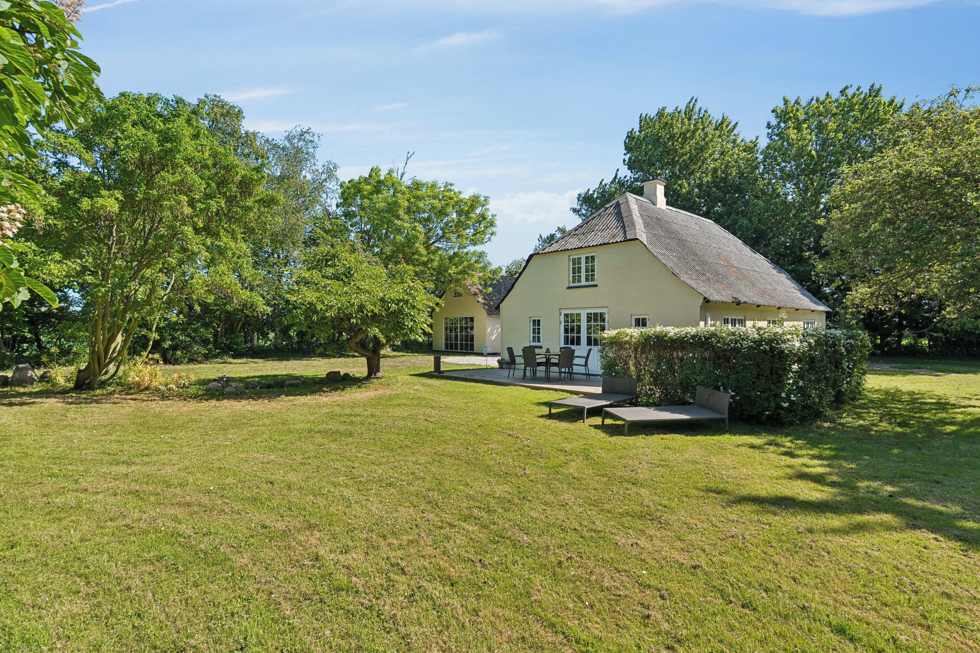 Ein Haus mit einem großen Rasen, einer Terrasse mit Gartenmöbeln und einem gepflegten Garten.